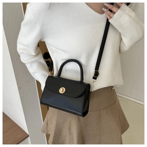 Model wearing black leather mini square bag with golden round lock and top handle