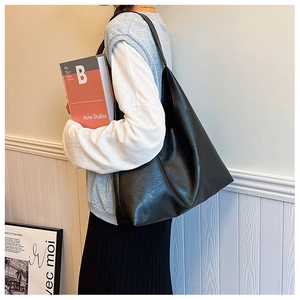 Close-up of a black oversized PU leather tote bag worn by a model in a minimal setting