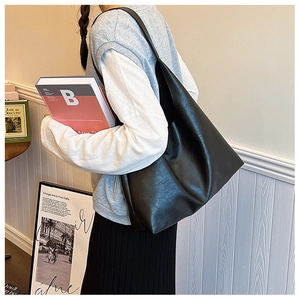 Minimalist large black leather tote bag worn by a model in a cozy lifestyle setting