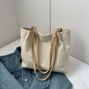 Off-white canvas tote bag with brick texture and brown leather straps on denim background