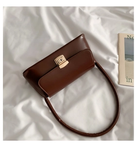 Détail d'un sac à bandoulière vintage marron foncé avec fermoir doré sur tissu blanc