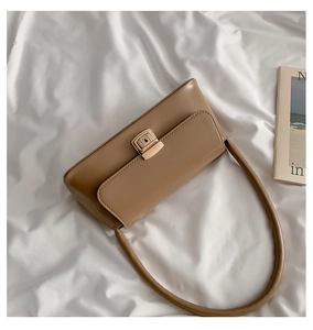 Détail du sac à bandoulière en cuir camel avec boucle métallique sur tissu blanc