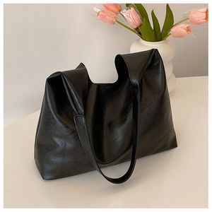 Close-up of black tote bag with soft leather texture on white table with tulips