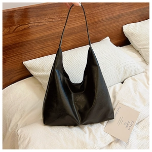 Minimalist black PU leather hobo tote bag with wide shoulder strap on white bedding