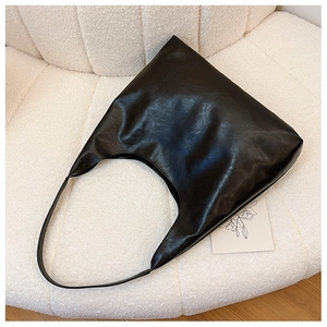 Detail of glossy black pleated leather texture and wide strap on minimalist tote bag