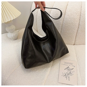 Close-up of large black Hobo bag with glossy leather texture on a white plush sofa
