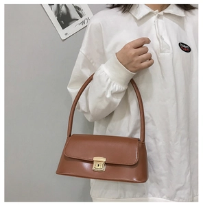 Détail du sac baguette en cuir caramel avec boucle dorée sur fond de chemise blanche