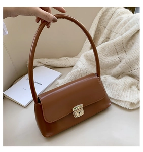 Détail du sac baguette en cuir marron caramel avec fermoir vintage doré sur un canapé