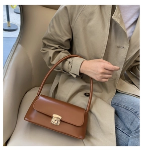 Détail du sac baguette en cuir marron avec boucle dorée sur un trench-coat chic