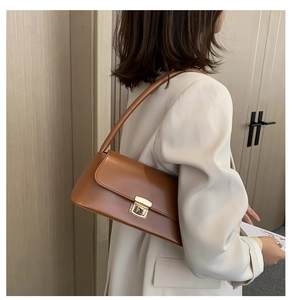 Détail d'un sac baguette en cuir souple marron avec boucle dorée porté sous le bras