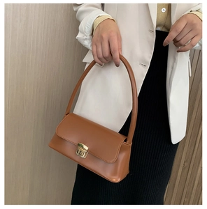 Détail du sac baguette camel avec boucle dorée tenu à la main par un mannequin