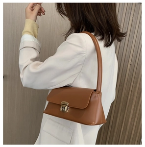 Sac baguette en cuir souple marron avec boucle dorée porté à l'épaule sur un blazer