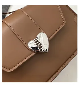 Close-up of brown leather bag featuring silver heart-shaped buckle and stitching detail