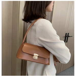 Sac baguette en cuir marron avec fermoir métallique doré sur un blazer crème