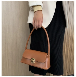 Gros plan d'un sac sous les bras marron caramel avec boucle dorée sur blazer blanc