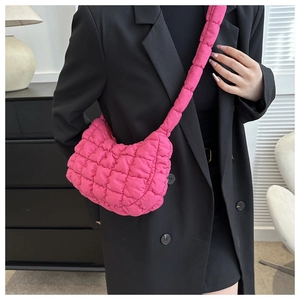 Close-up of bright pink quilted crescent bag with padded shoulder strap on black blazer