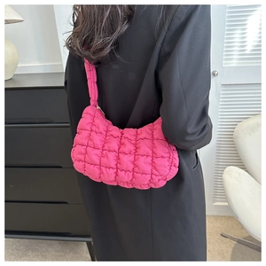 Detail of rose red quilted puffer bag with textured grid pattern and thick strap on model