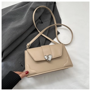 Close-up of beige crossbody bag featuring heart-shaped silver buckle and fine stitching