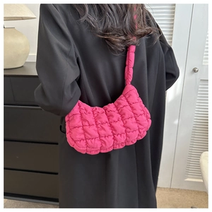 Detailed quilted texture of a vibrant magenta puffer shoulder bag worn by a model