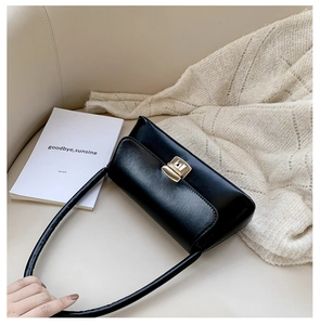 Détail du sac baguette en cuir noir brillant avec un fermoir rotatif doré sur un canapé