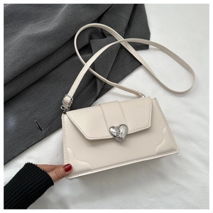 Detail showing cream crossbody bag with silver heart-shaped buckle and fine stitching