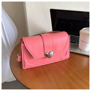 Detailed shot of pink leather crossbody bag with silver heart buckle on wooden table