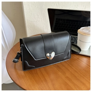 Detail of black crossbody bag with silver heart-shaped clasp on a wooden table