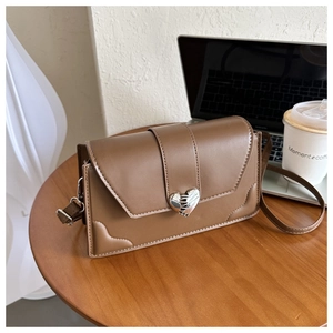 Close-up of brown PU leather crossbody bag with metallic cracked heart buckle on wooden desk