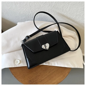 Detail of a black rectangular crossbody bag with a silver heart buckle on a white jacket