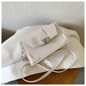 Detail of cream crossbody bag with silver heart clasp and wavy stitching on a blazer