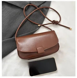 Detail of dark brown leather crossbody bag with flap closure and knot strap accents