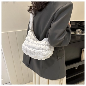 Detailed side view of a white quilted puffer shoulder bag worn by a model in a modern room
