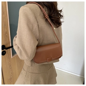 Detail view of a brown minimalist leather underarm bag with knot strap and square buckle