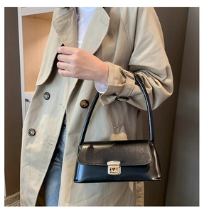 Détail d'un sac bandoulière noir avec fermoir métallique porté sur un manteau beige