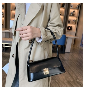 Détail du sac baguette noir avec boucle dorée et finition en cuir poli sur trench-coat