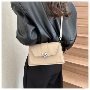 Side view of a chic cream heart-clasp crossbody bag on a model in a minimal setting