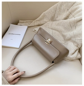 Détail du sac bandoulière en cuir mat chameau avec fermoir doré sur un canapé