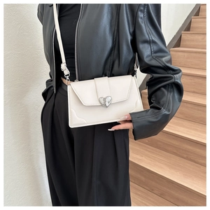 Detail of cream crossbody bag featuring a silver heart-shaped clasp and textured metal