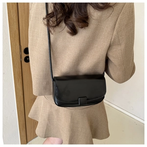 Detail of minimalist black crossbody bag on model with square buckle and smooth texture