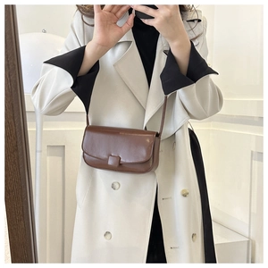 Brown leather crossbody flap bag with square buckle detail on beige trench coat