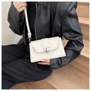 Detail of a beige crossbody bag with textured silver heart clasp and fine stitching
