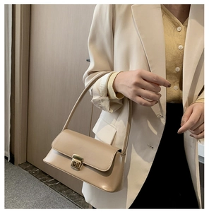 Détail d'un sac à bandoulière en simili cuir beige avec boucle dorée porté par un modèle