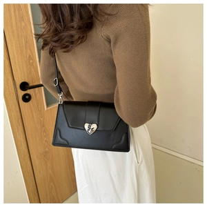 Detail of a black leather crossbody bag with a silver heart buckle on a female model