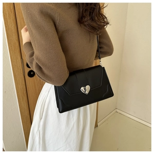 Side view of a black square crossbody bag with a silver heart-shaped metal clasp