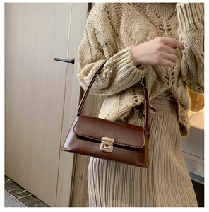 Détail d'un sac sous le bras marron vintage en cuir avec boucle dorée porté sur un pull-over