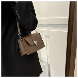 Brown faux leather crossbody bag with silver heart clasp shown on a shoulder