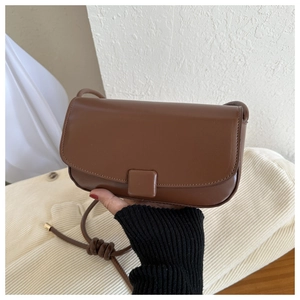 Detail of a dark brown matte leather flap bag with thin strap and metallic accents