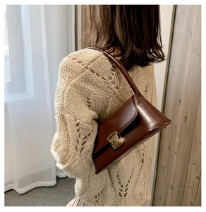Détail d'un sac à bandoulière marron foncé avec boucle dorée porté par un mannequin