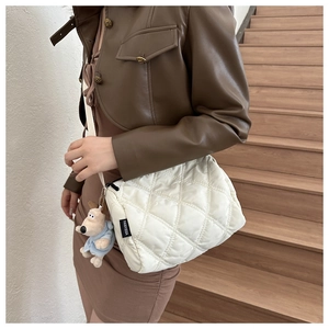 Detail of off-white quilted puffer bag with a blue dog plush keychain on the strap