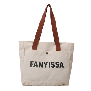Minimalist beige canvas tote bag with FANYISSA print and brown woven handles on white base